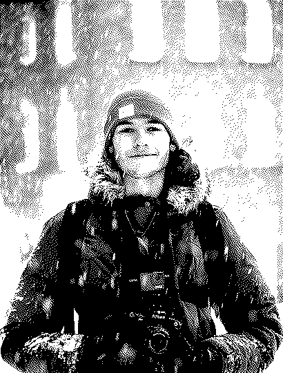 Felix smiling in falling snow, wearing a beanie and parka, with cameras on his chest strap.